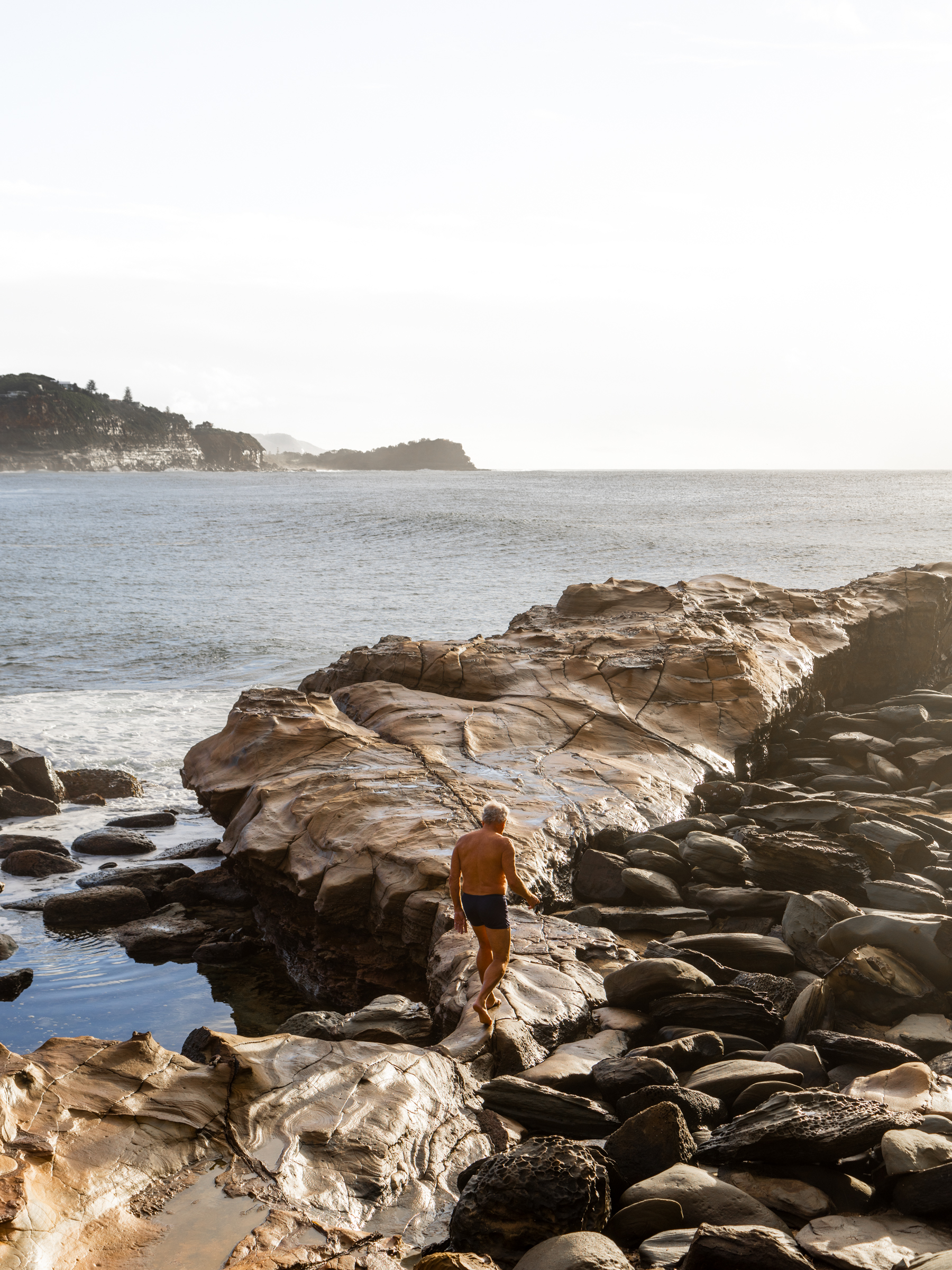 Early morning swimmer walking along the rocks to the ocean